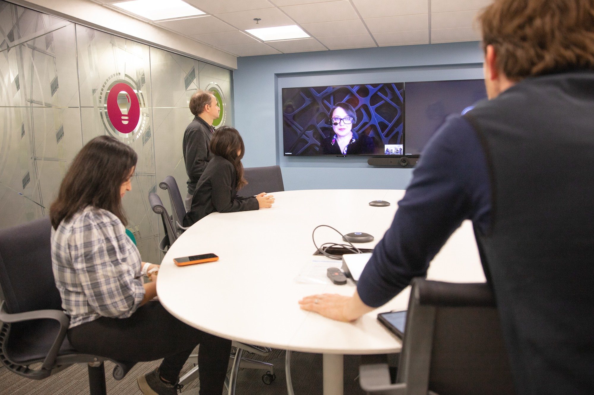 Four researchers gather around a table and talk to a virtual participant on a large monitor.