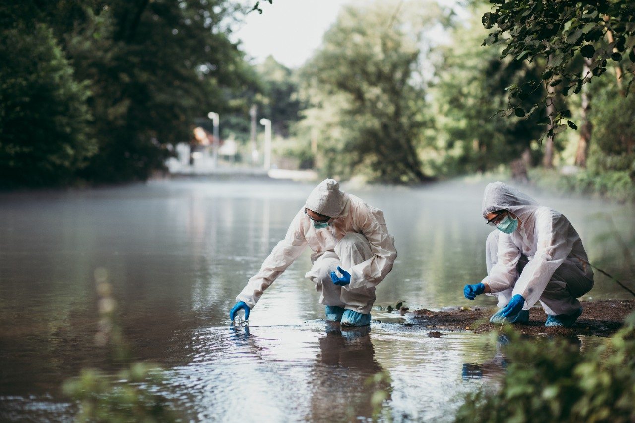 Two scientists in protective suits taking water samples from river