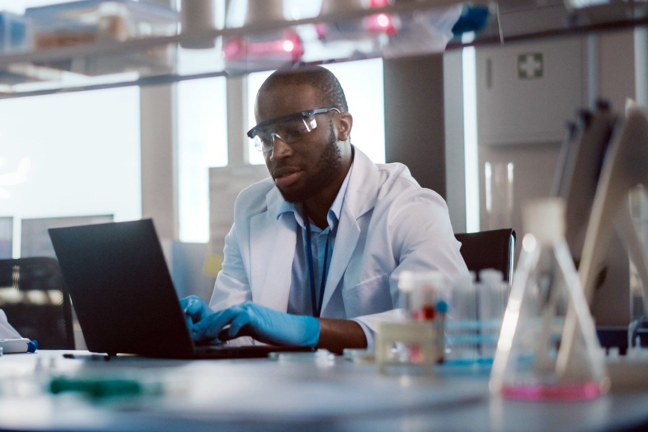 Research scientists working in lab on laptop in PPE